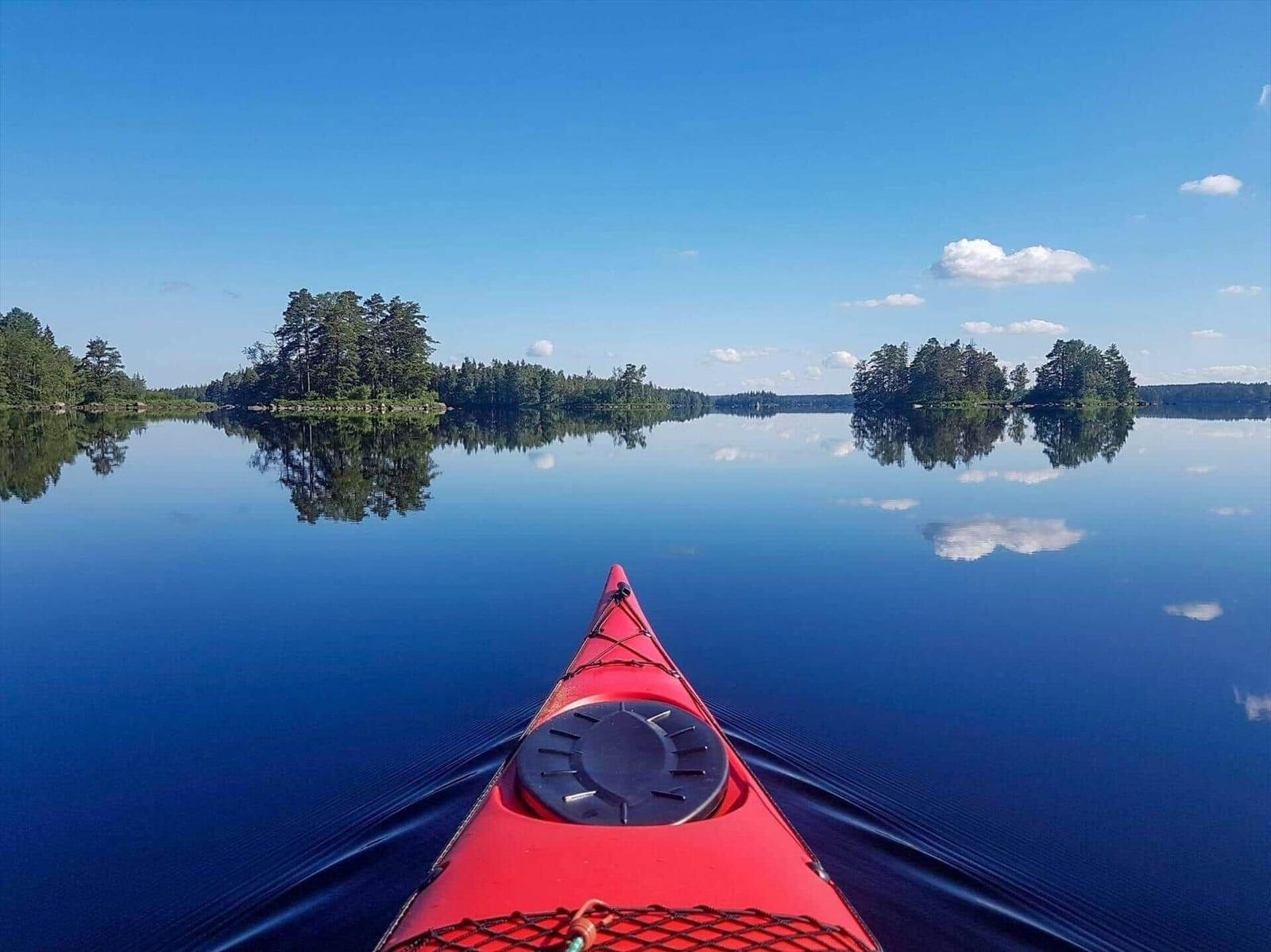 Roter Kajak auf ruhigem See mit Waldinseln und blauem Himmel.