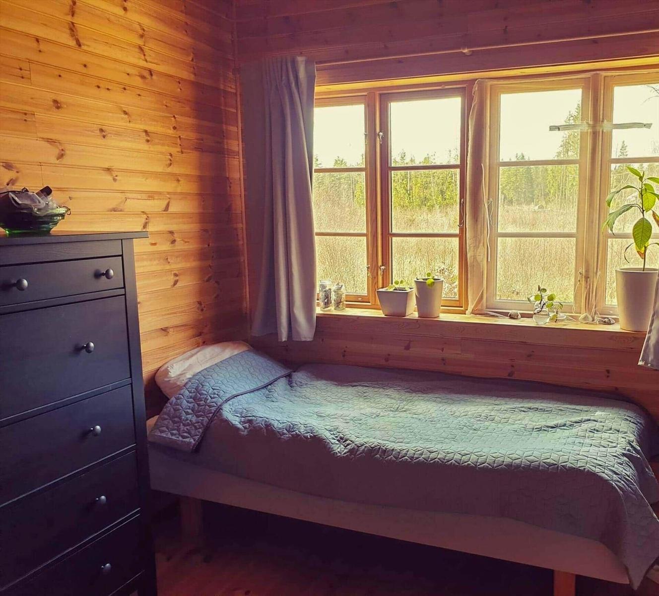 Ein Schlafzimmer mit Holzwand, Bett und Fenster mit Pflanzen.