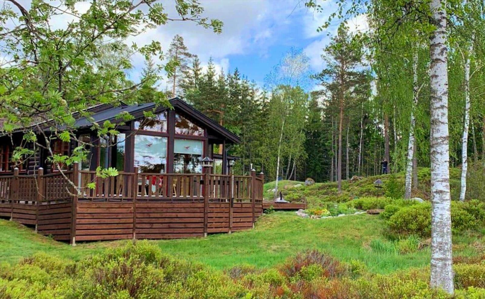 Holzhütte mit Balkon im Wald. Grünflächen und Bäume umgeben das Haus.