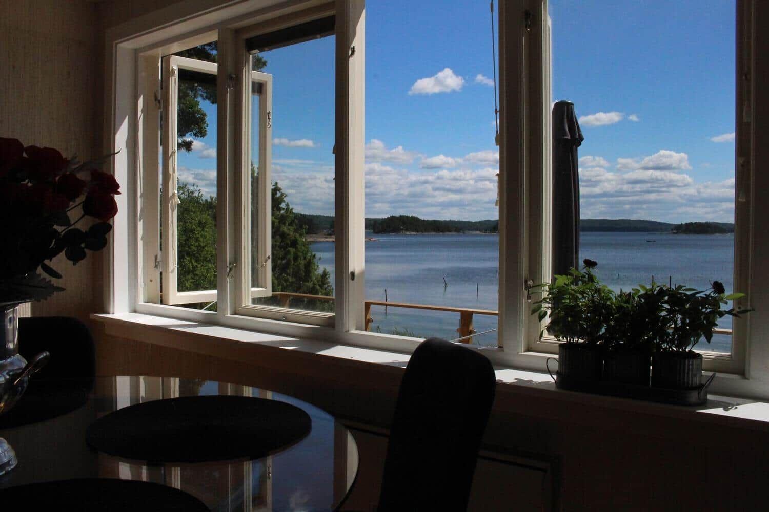 Durch das Fenster blickt man auf einen See mit Bäumen und einem Balkon.