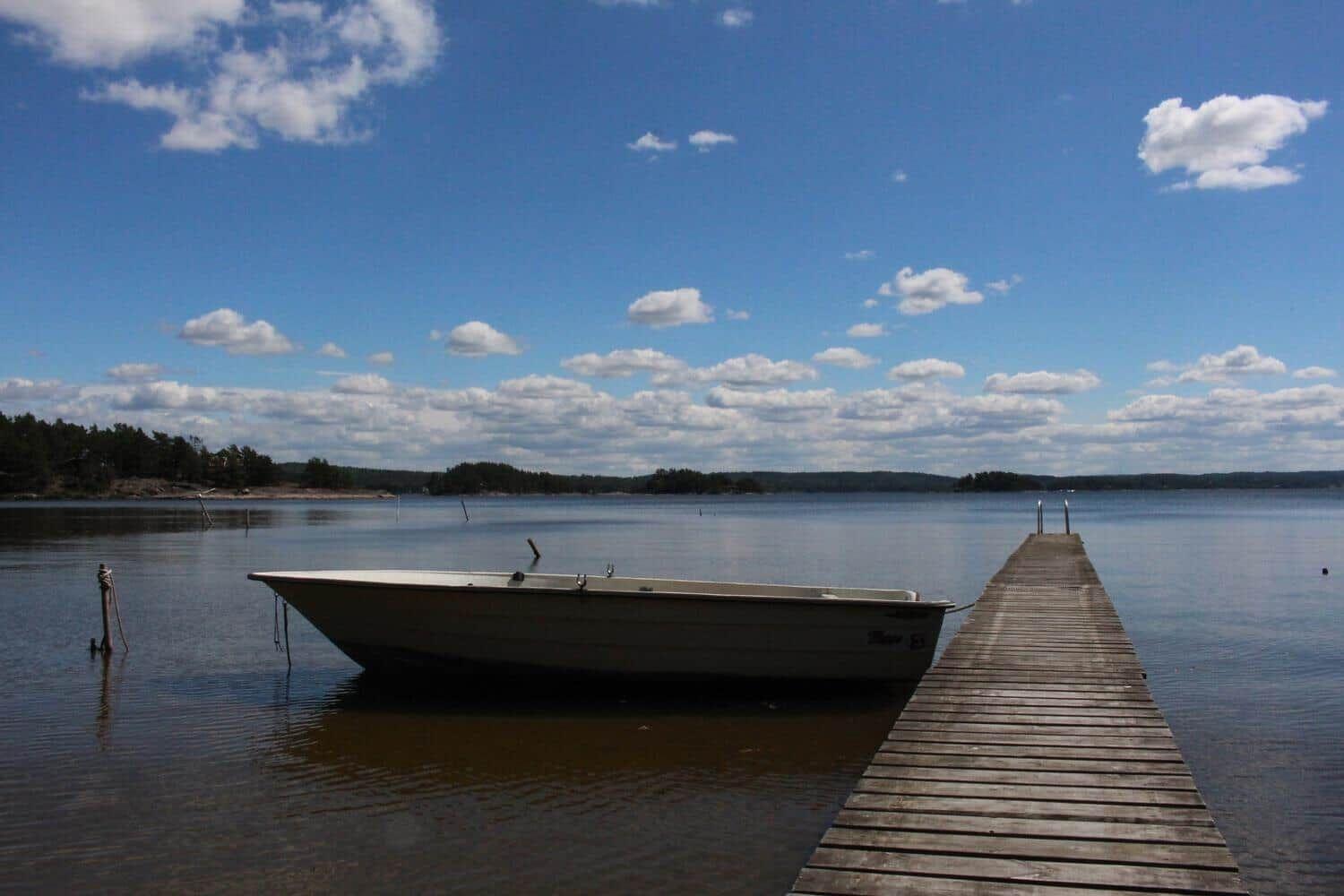 Ein kleines Boot liegt am Steg eines Sees mit bewölktem Himmel.
