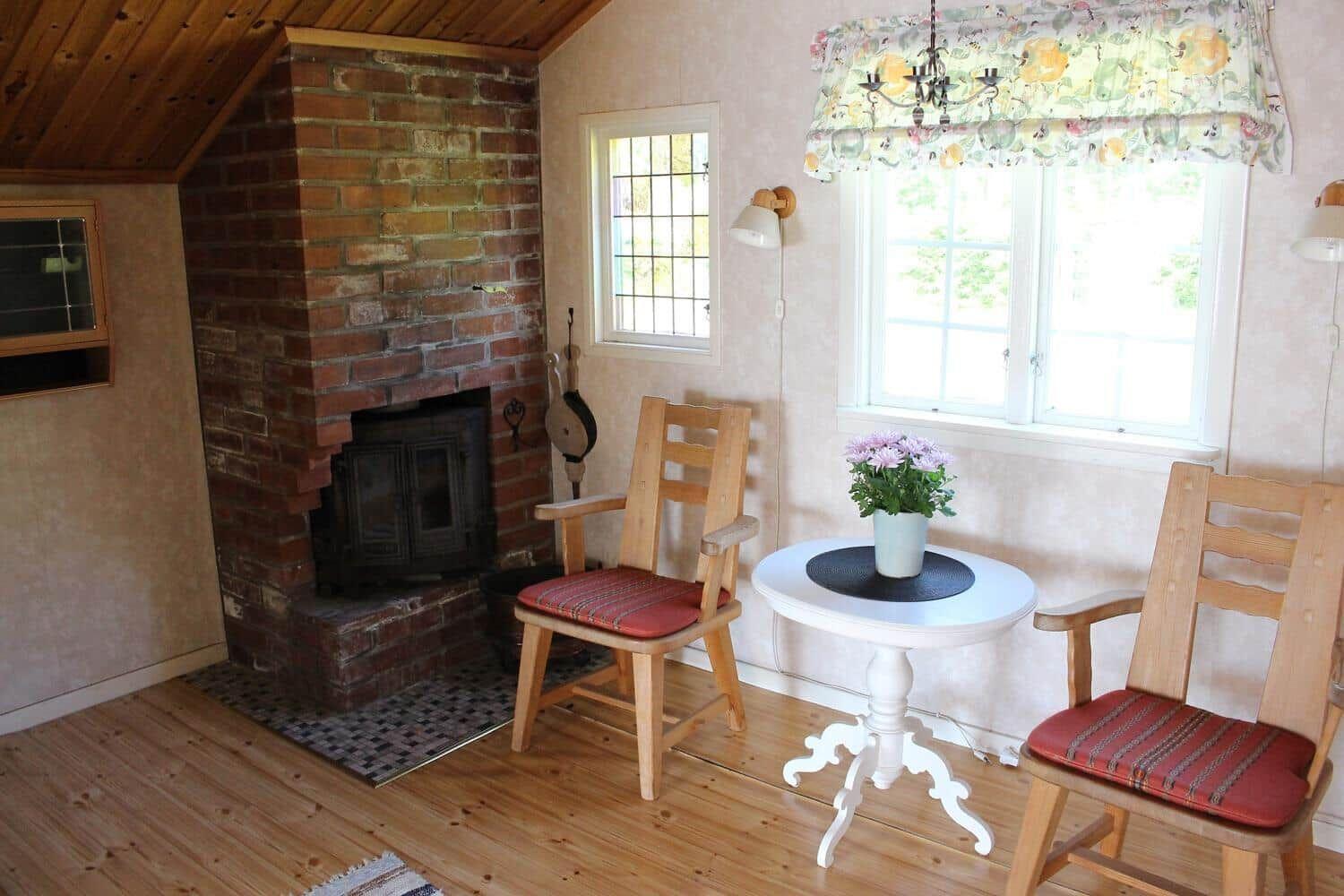 Raum mit Kamin, Tisch und zwei Stühlen vor Fenster.