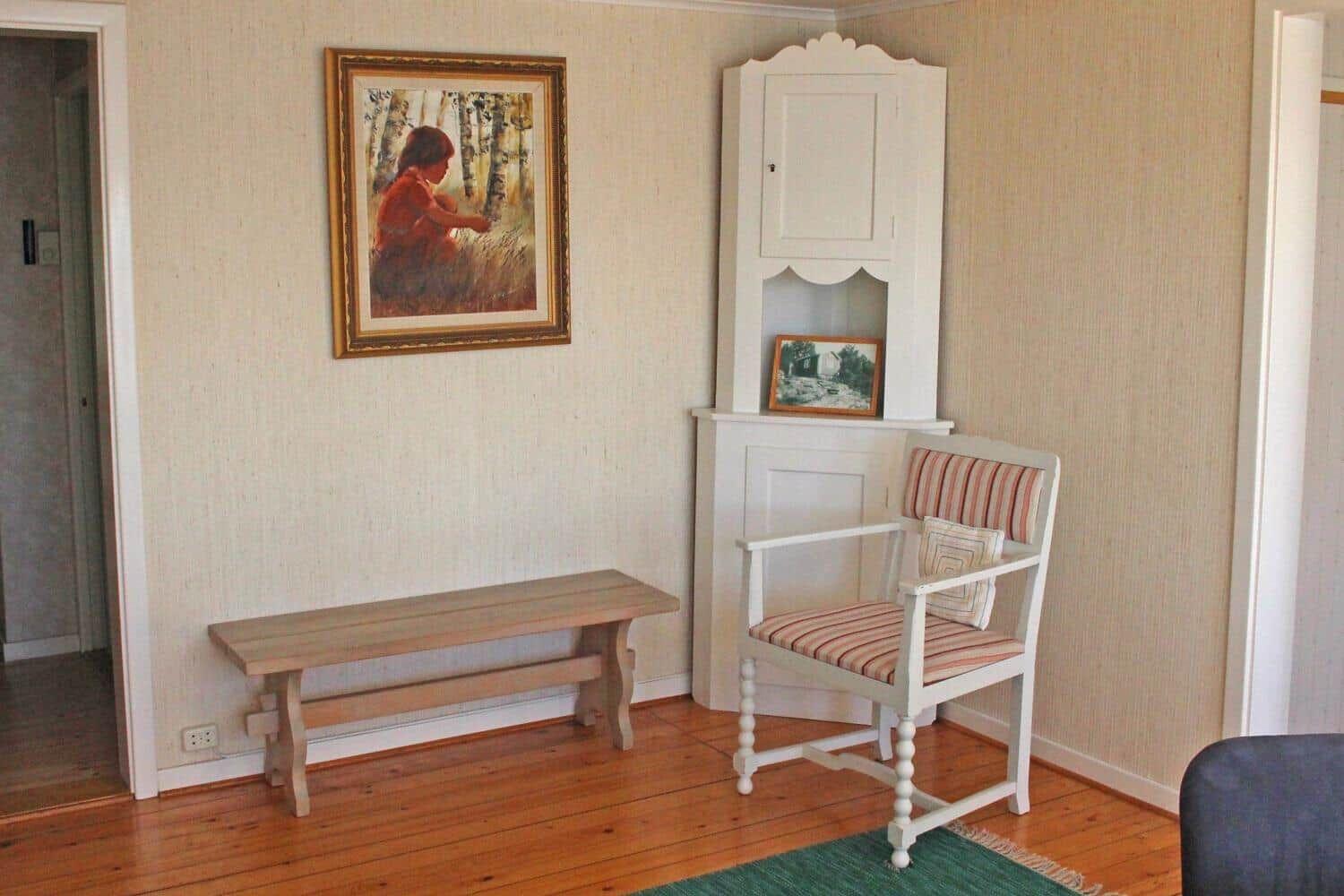 Raum mit Holzboden, Stuhl und Bank. Wandbild und weißer Schrank sind sichtbar.