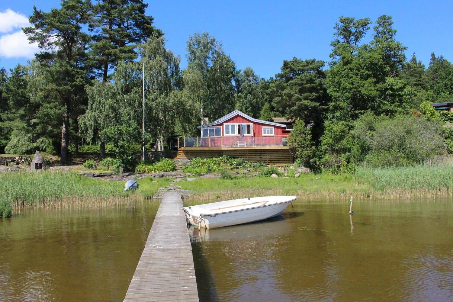 Rotes Haus am See mit Bootssteg und weißen Boot.