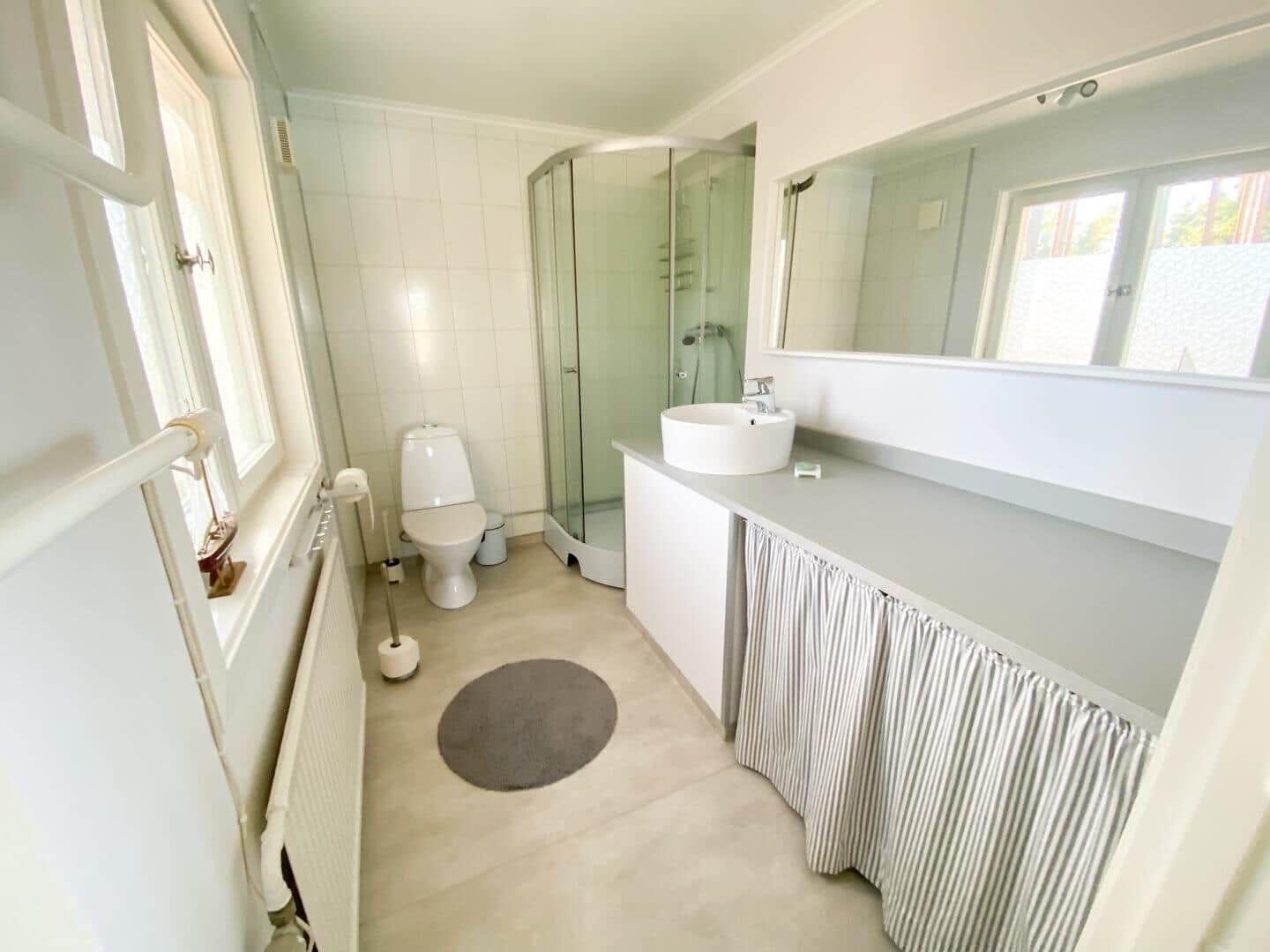 Badezimmer mit Dusche, Waschbecken und Toilette. Fenster und Spiegel sichtbar.