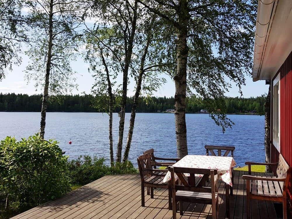 Terrasse mit Tisch und Stühlen am See. Blick auf Wasser und Bäume.