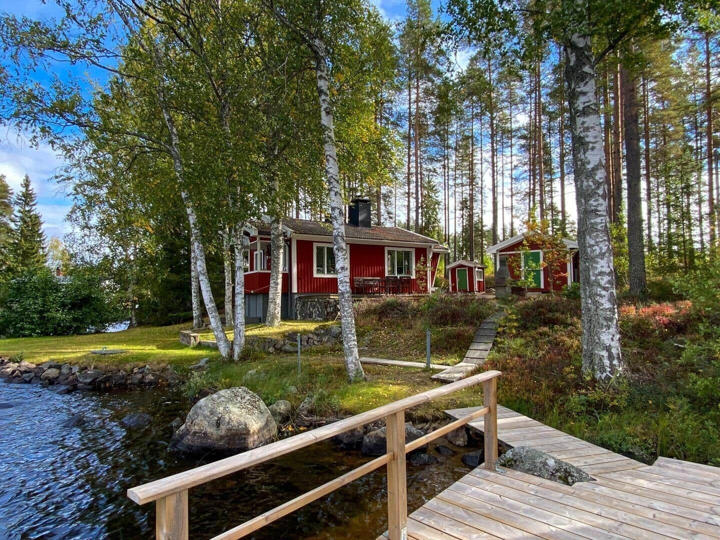 Rotes Holzhaus am See mit Holzsteg und Bäumen