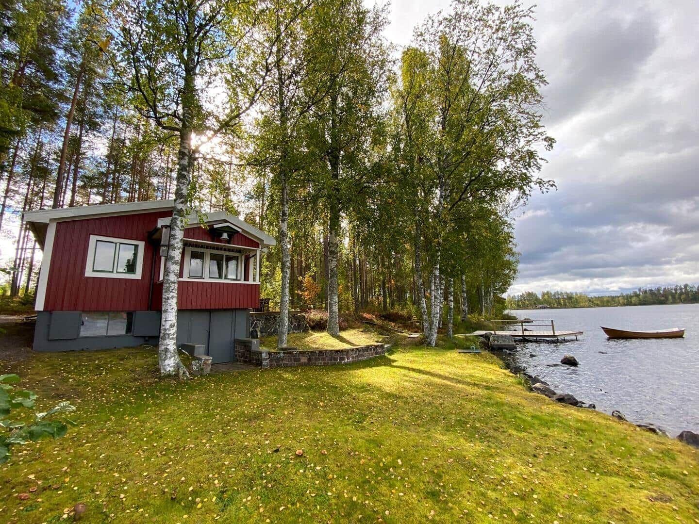 Rotes Haus am See mit Boot und Bäumen