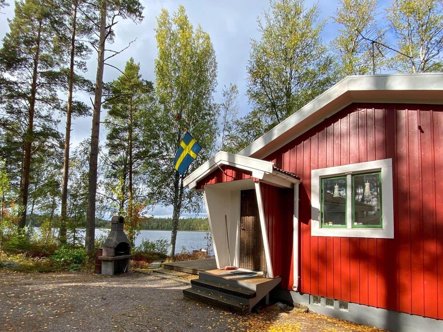 Rotes Holzhaus mit Schwedenflagge, Grill und Seeblick.