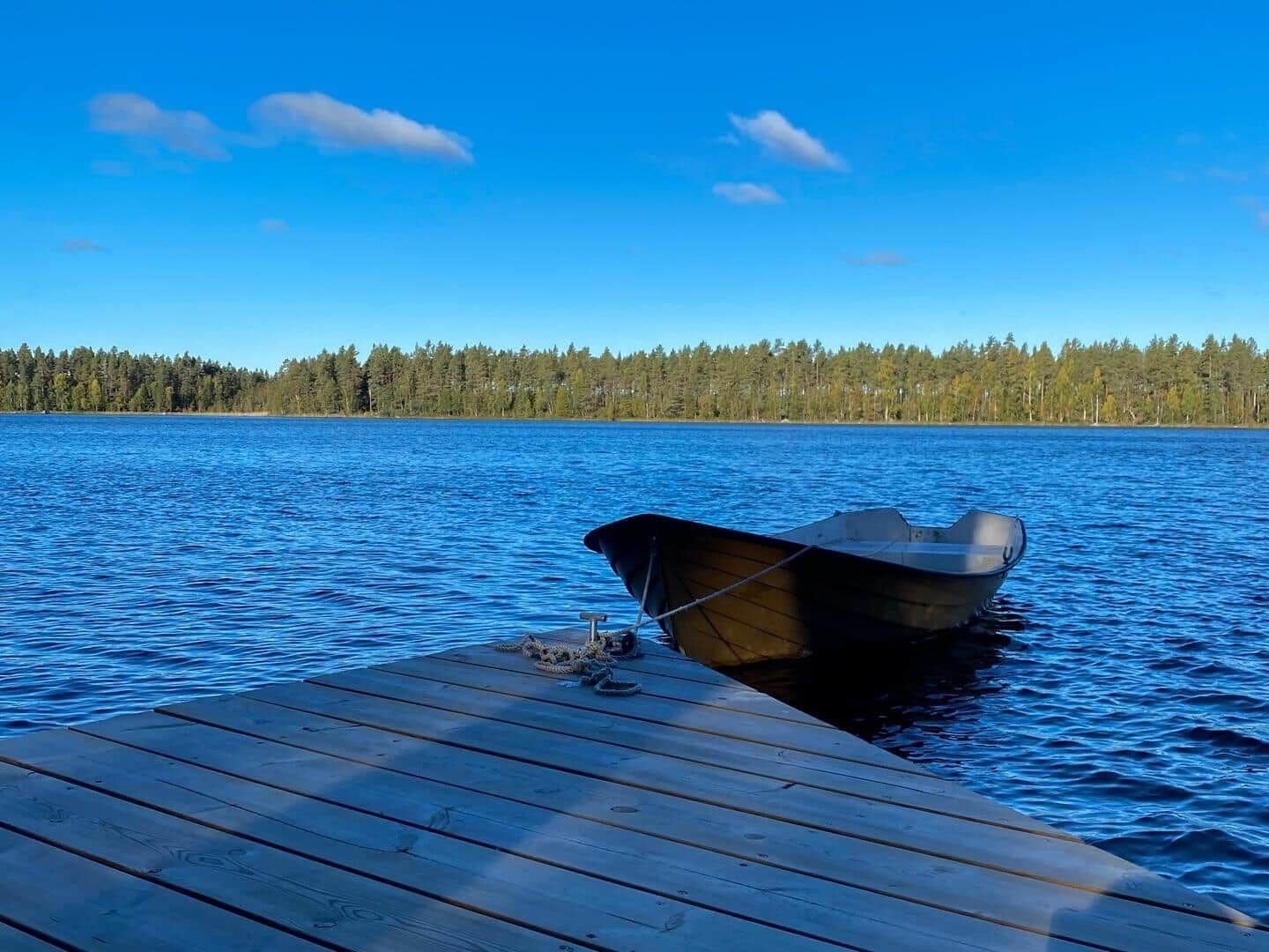 Ein kleines Boot liegt am Holzsteg eines Sees mit Wald im Hintergrund.