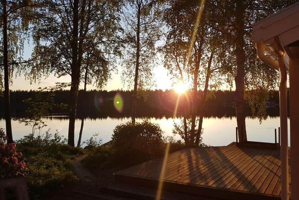 Sonnenuntergang über See mit Holzterrasse und Bäumen