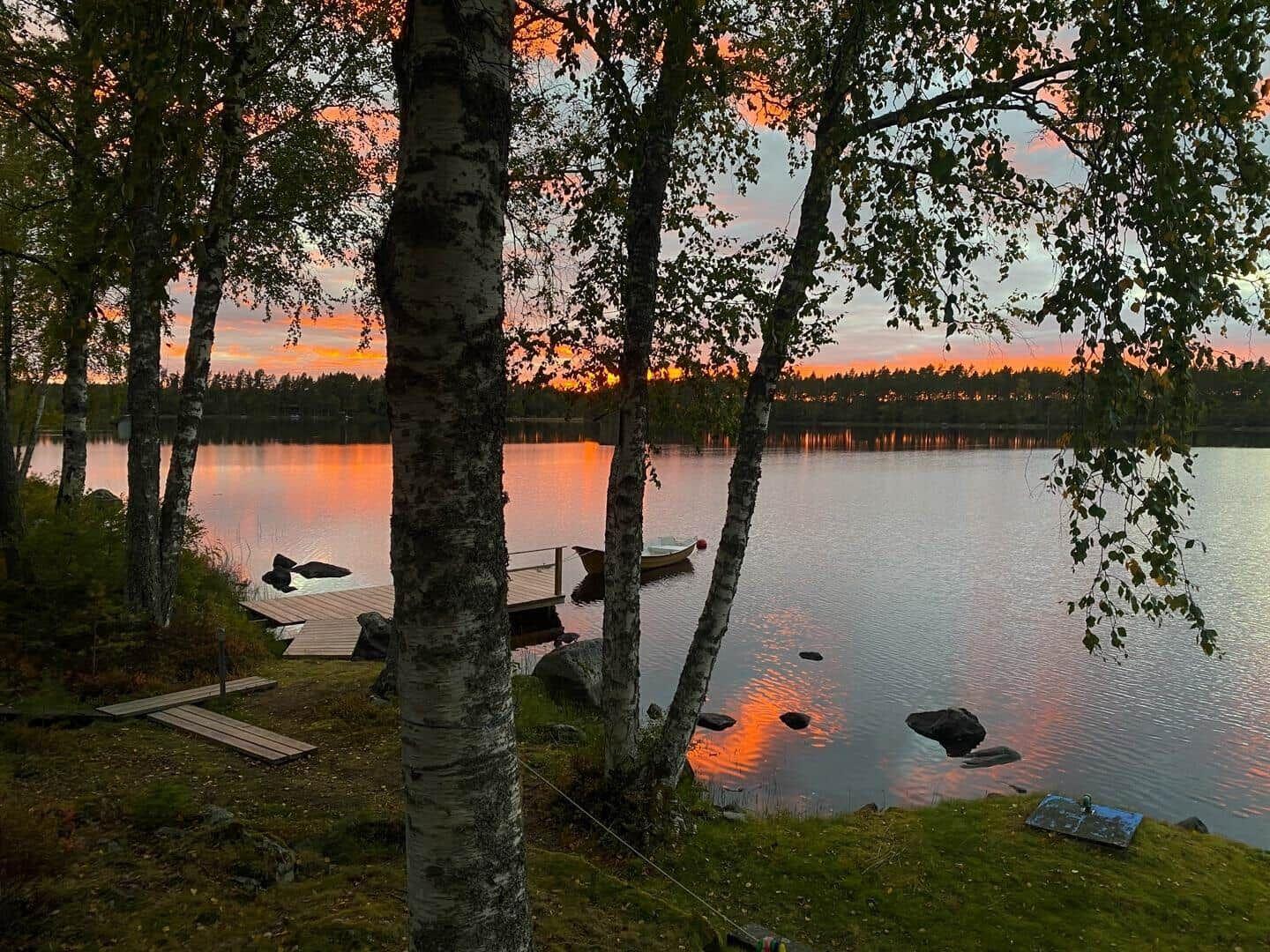 Lakeside-View mit Birken, Boot und Sonnenuntergang.