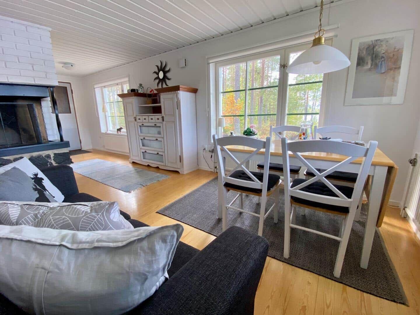 Wohn- und Essbereich mit Kamin, Tisch und Stühlen, Fenster mit Blick auf Wald.