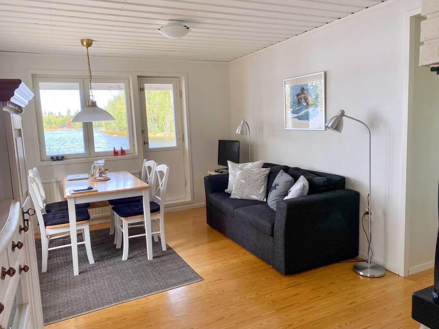 Wohn- und Essbereich mit Sofa, Tisch und Blick auf Wasser.
