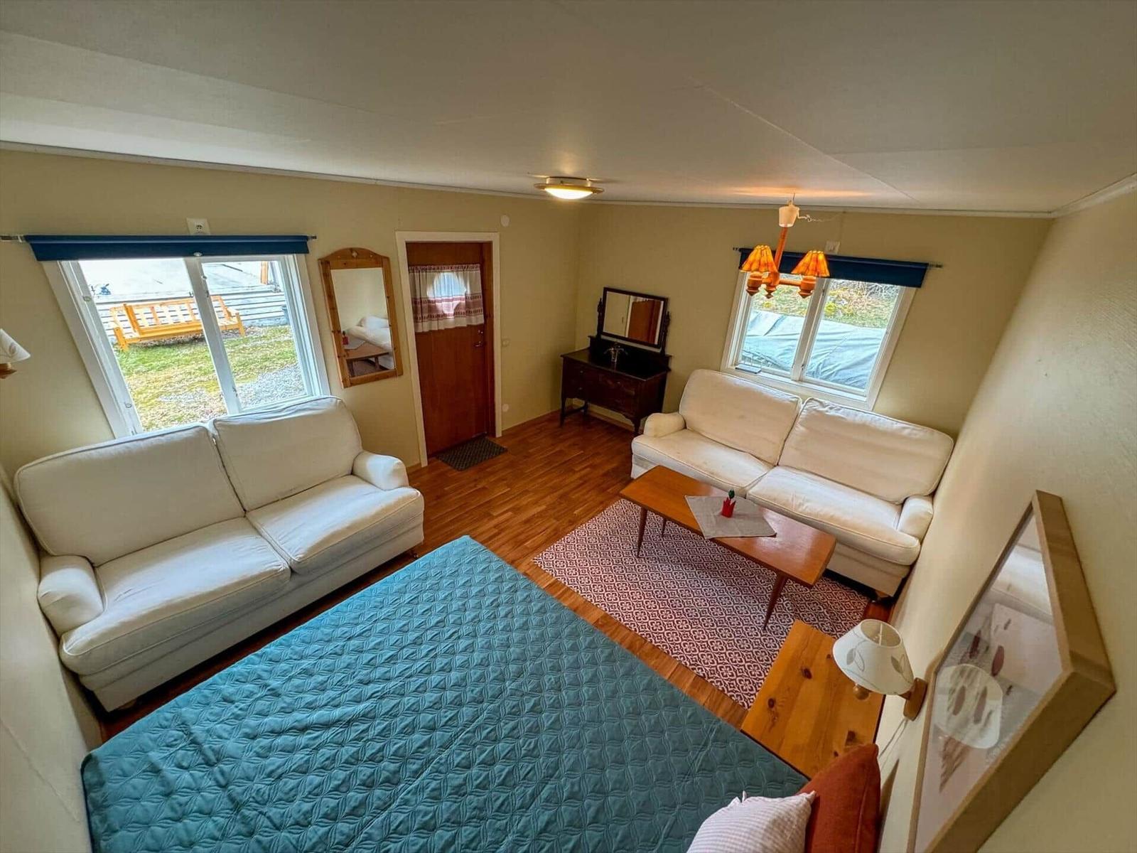 Wohnraum mit zwei Sofas, Bett und Holzboden. Fenster und Tür sichtbar.