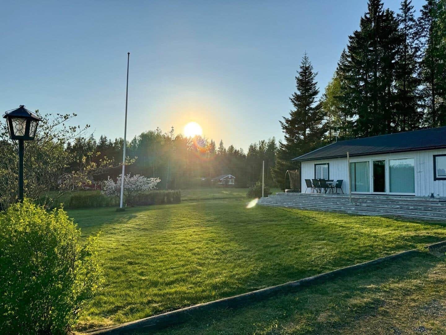 Wohnhaus mit Terrasse, Grasfläche und Wald im Hintergrund bei Sonnenuntergang.