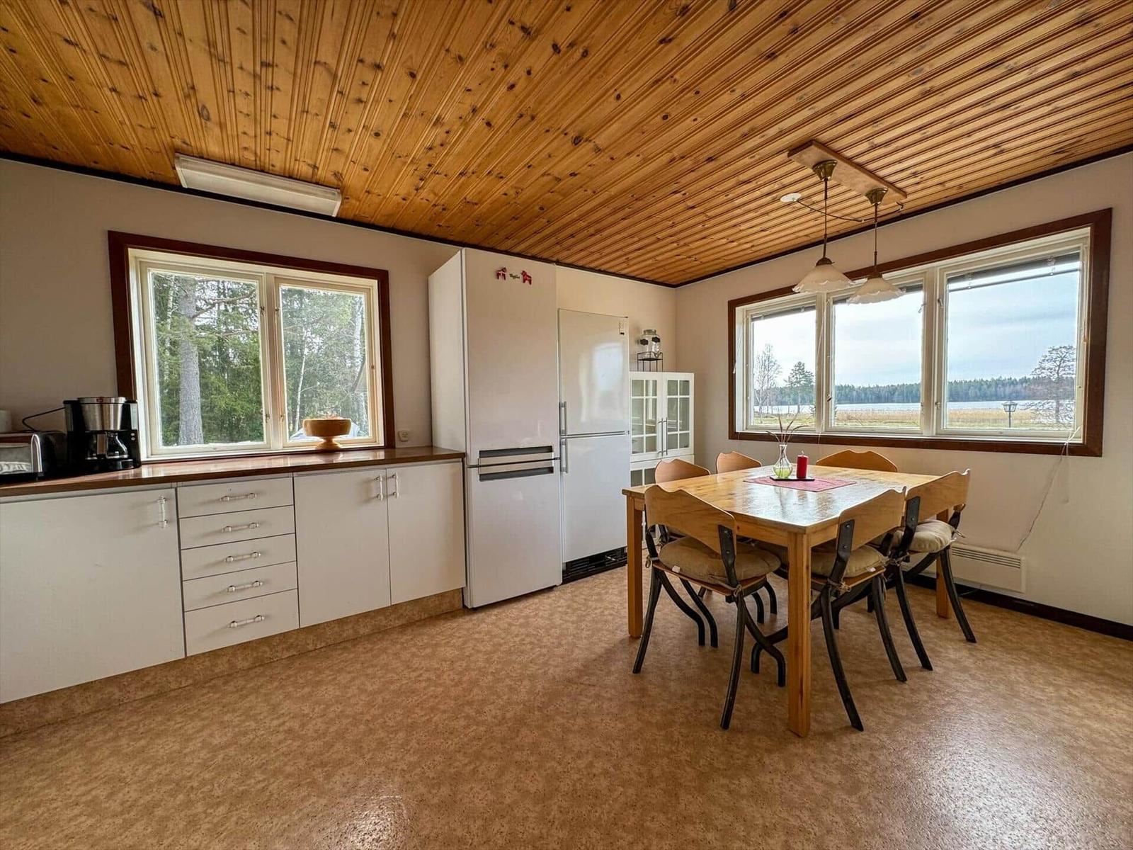 Küche mit Esstisch, Kühlschrank und Fenstern mit Blick auf Wald und Wasser.