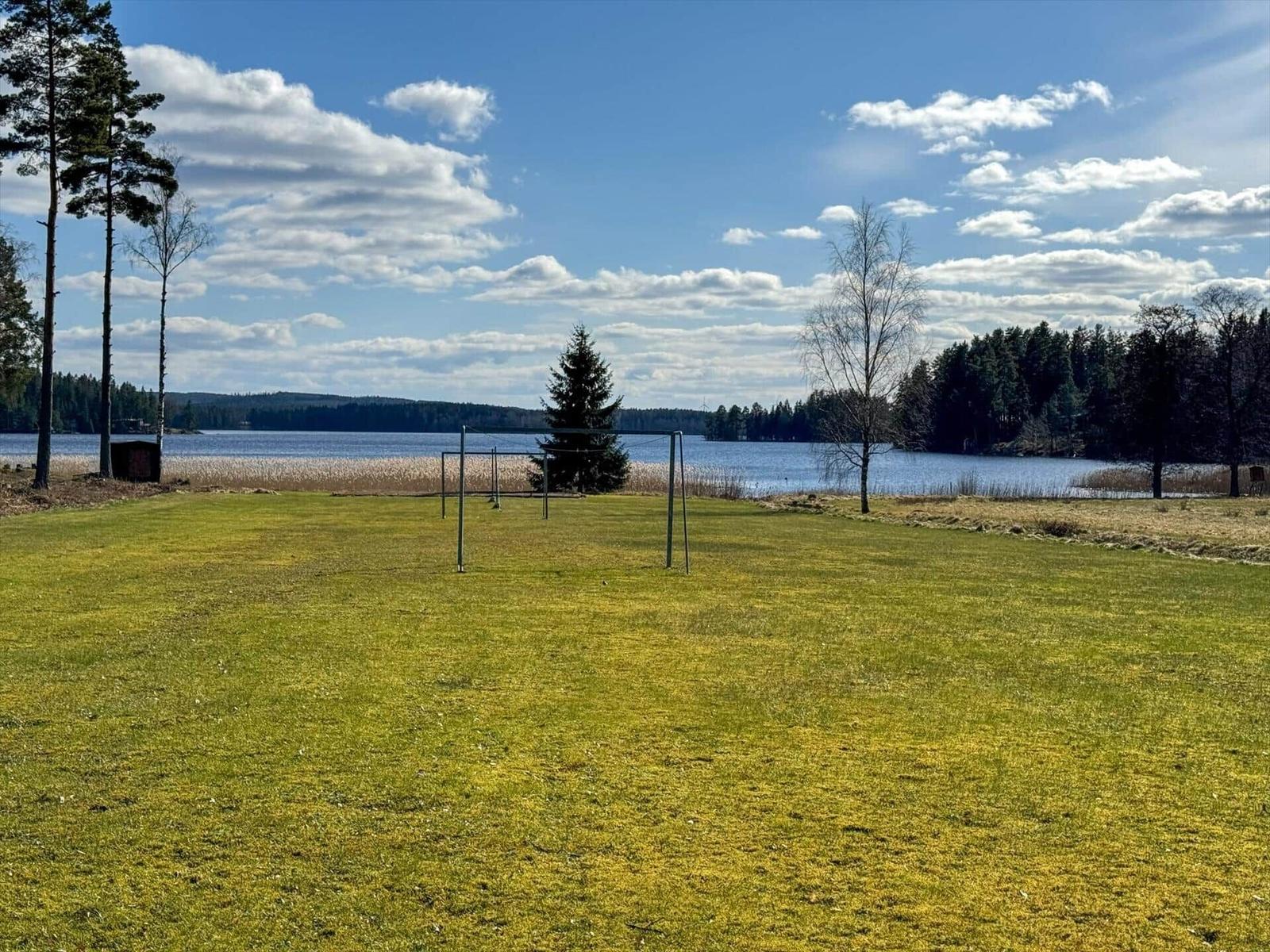 Grünes Feld mit Tor vor See und Wald.
