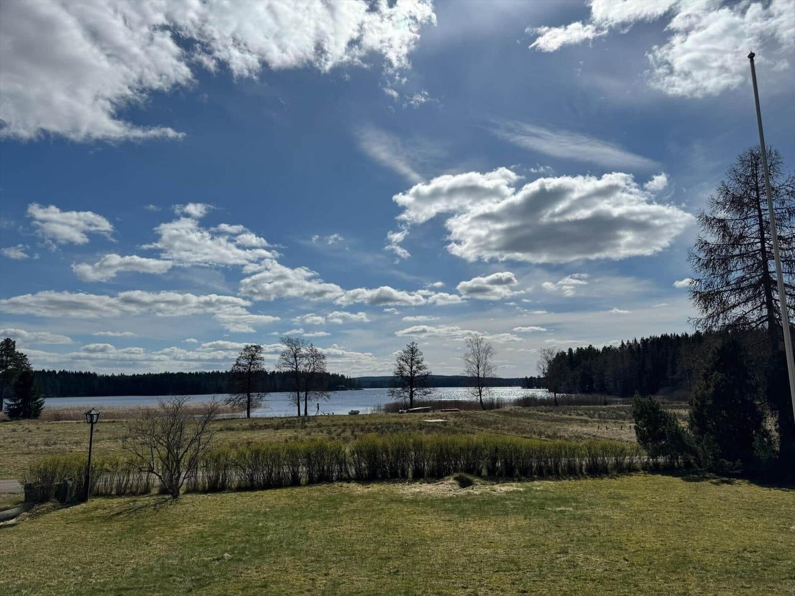 Weiterer Blick auf den See mit Bäumen und bewölktem Himmel.
