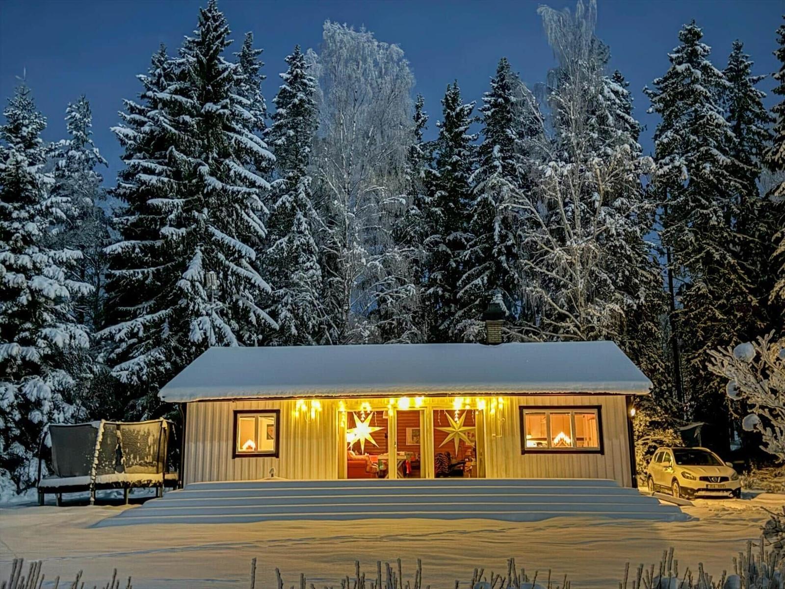 Wohnhaus mit Schnee, beleuchteten Fenstern und Türen im Winterwald.