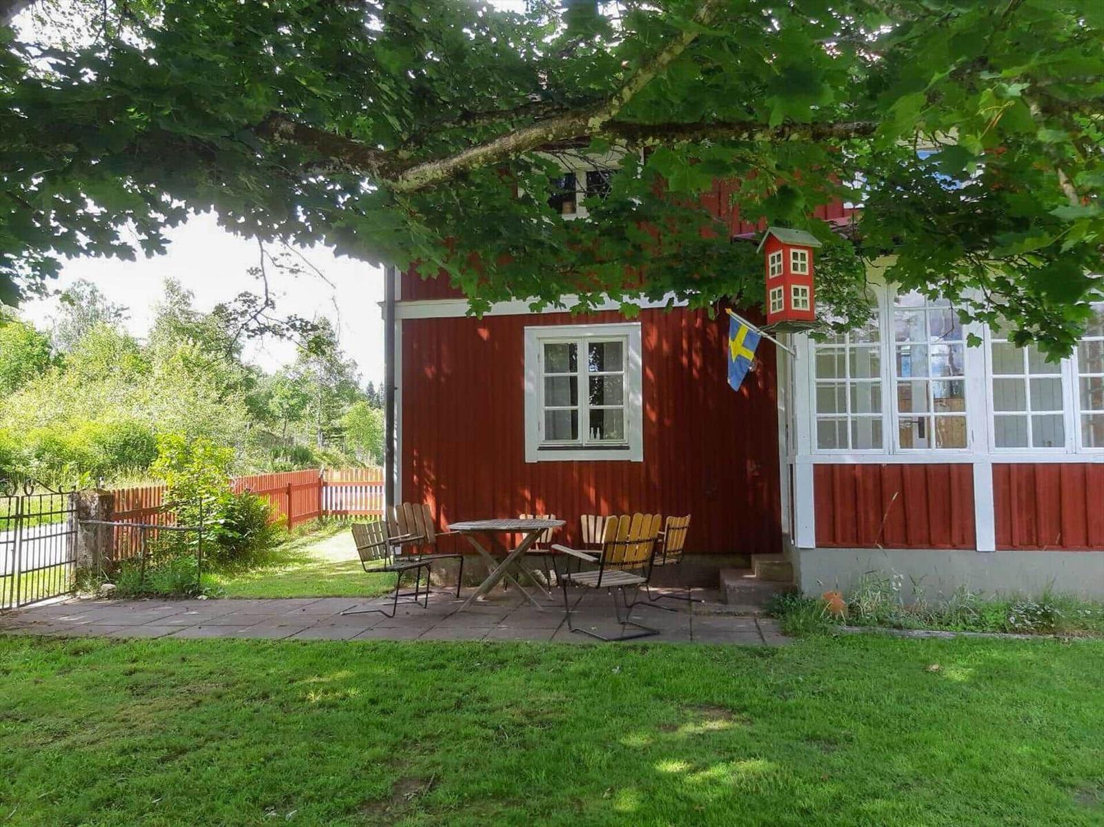 Rotes Holzhaus mit Terrasse, Tisch und Stühlen unter Bäumen.