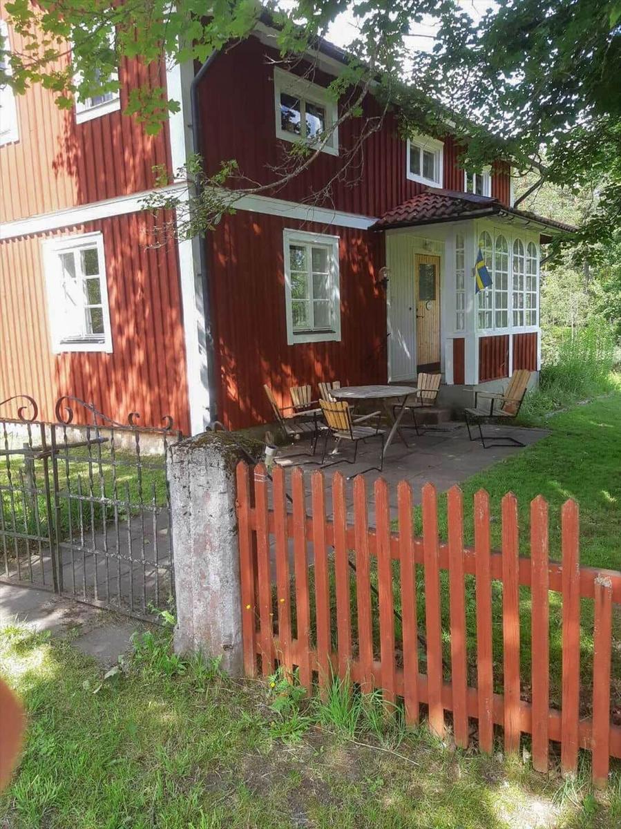 Rotes Holzhaus mit Terrasse und Gartenzaun. Schwedische Flagge an der Tür.