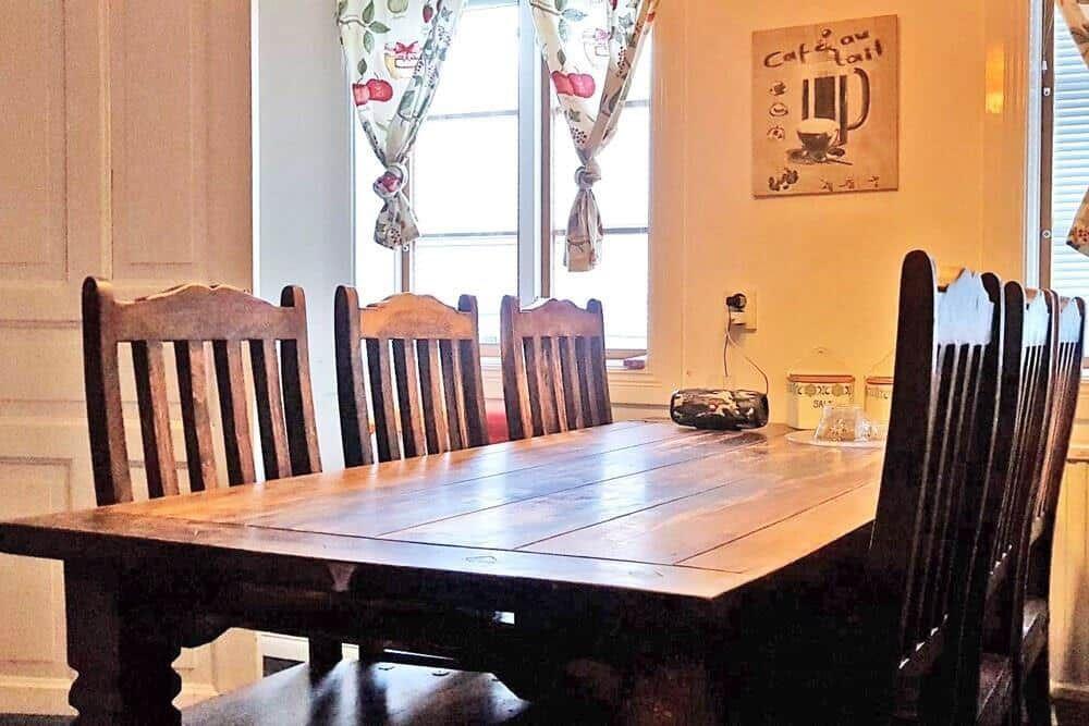 Holztisch mit sechs Stühlen vor Fenster mit Vorhängen