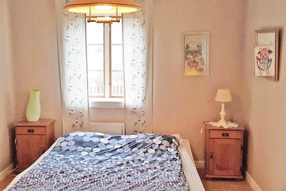 Schlafzimmer mit Bett, zwei Nachttischen und Fenster mit Vorhängen.