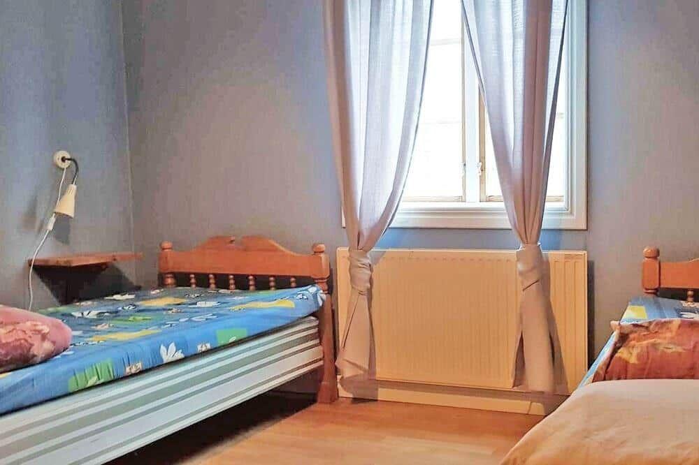 Zwei Betten mit bunten Bettwäschen, Fenster mit Vorhängen und Heizkörper.