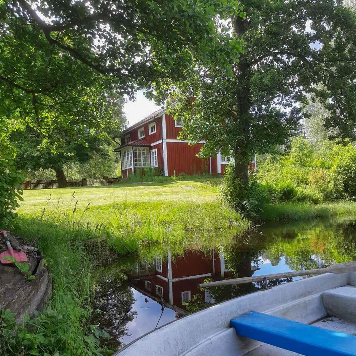 Rotes Haus mit grünem Garten und Wasserreflexion. Boot im Vordergrund.