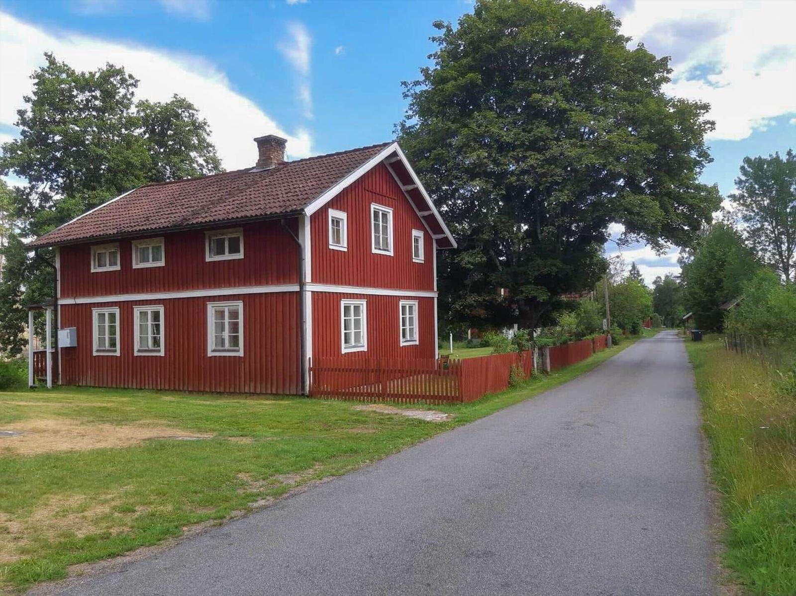 Rotes Holzhaus mit weißen Fenstern und rotem Zaun entlang einer Straße.