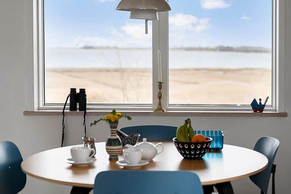 Runder Tisch mit Stühlen vor großem Fenster mit Blick auf Wasser.