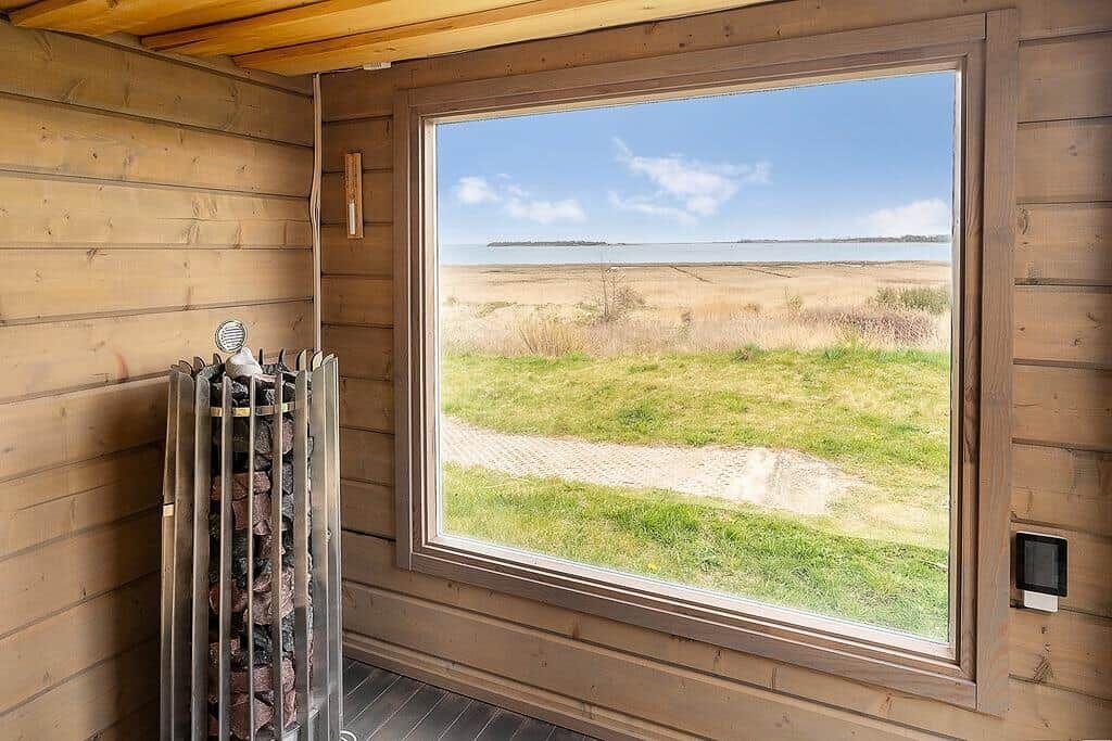 Holzverkleidete Sauna mit Blick auf Feld und Wasser.