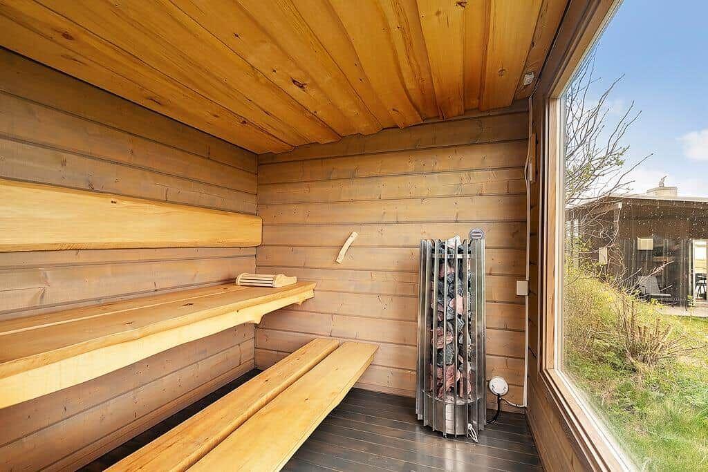 Holzsauna mit Sitzbänken und Ofen. Blick auf Garten durch Fenster.