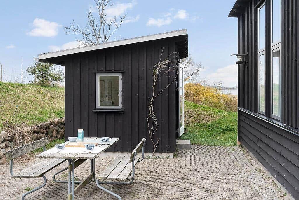 Außenbereich mit Tisch, Bänken und kleinem Haus neben großem Gebäude.
