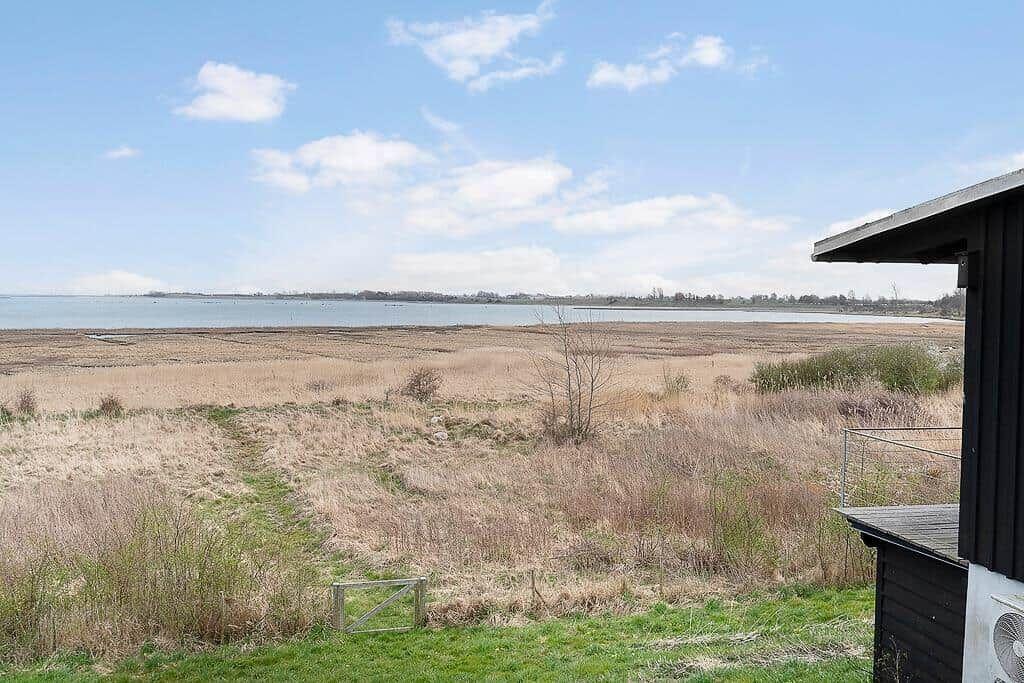 Weitläufiger Blick auf einen See mit trockenem Ufer und einem schlichten Holzhaus.
