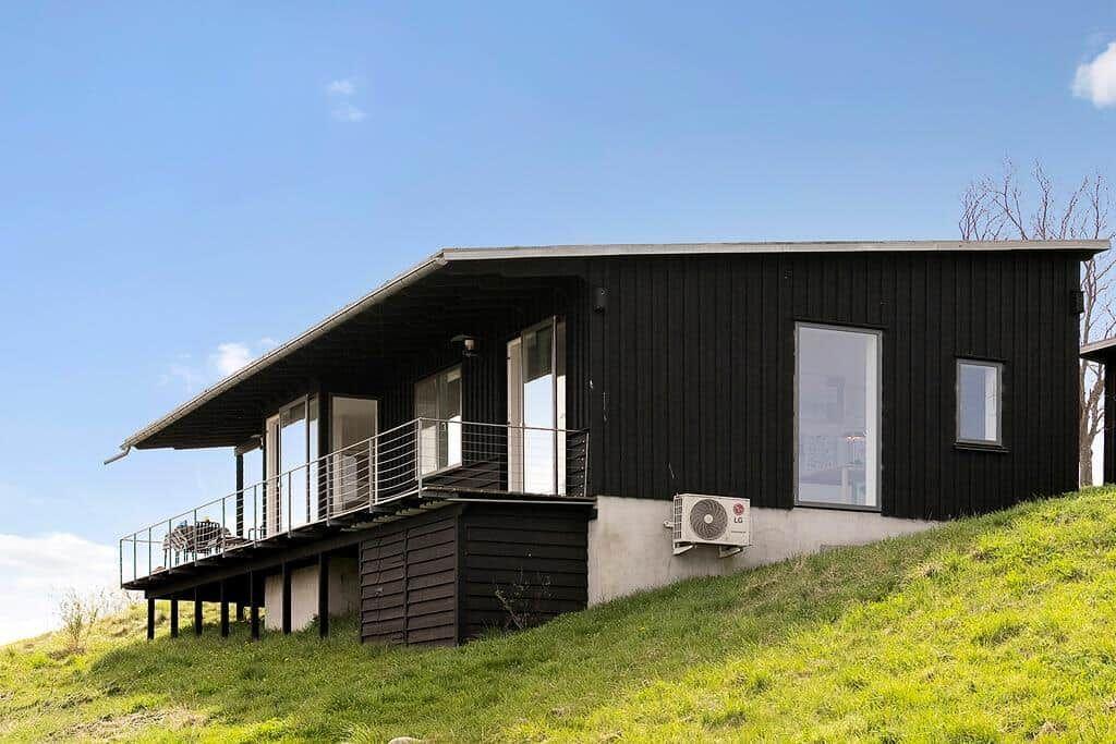 Moderne schwarze Hütte mit Balkon auf grüner Hanglage unter blauem Himmel.