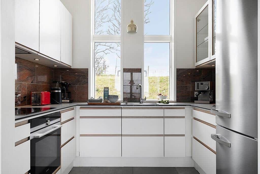 Moderne Küche mit weißen Schränken, Edelstahlgeräten und großem Fenster.