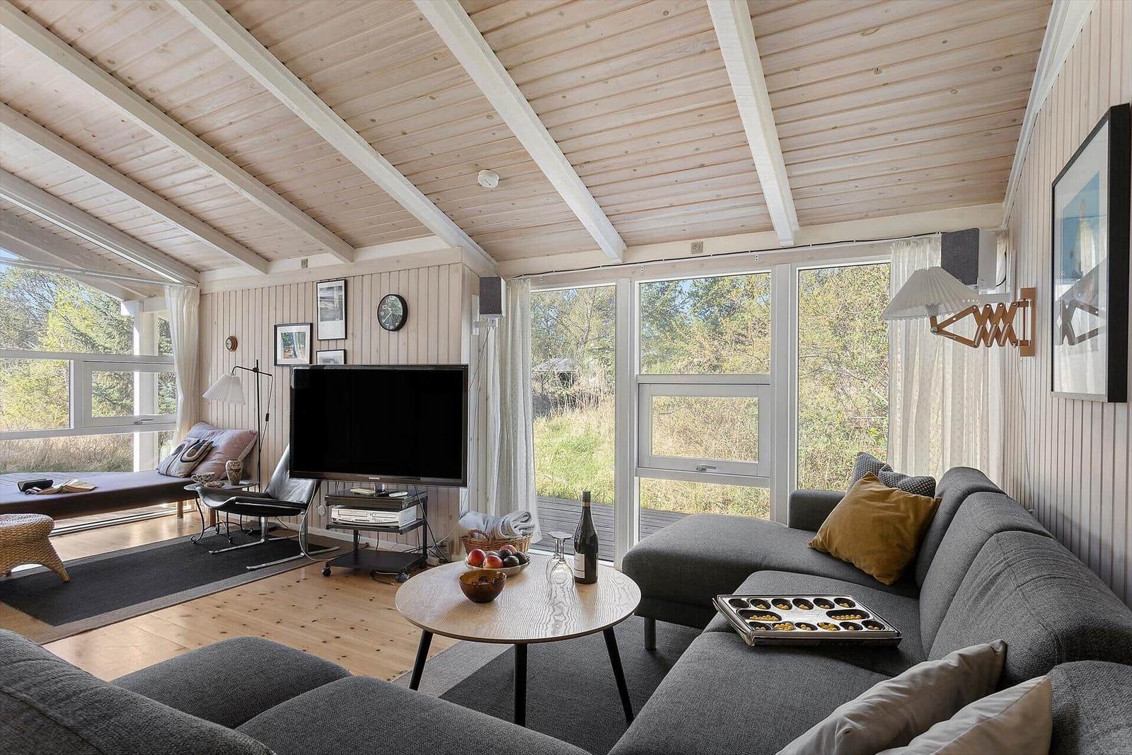 Wohnzimmer mit Sofa, Fernseher und großen Fenstern.