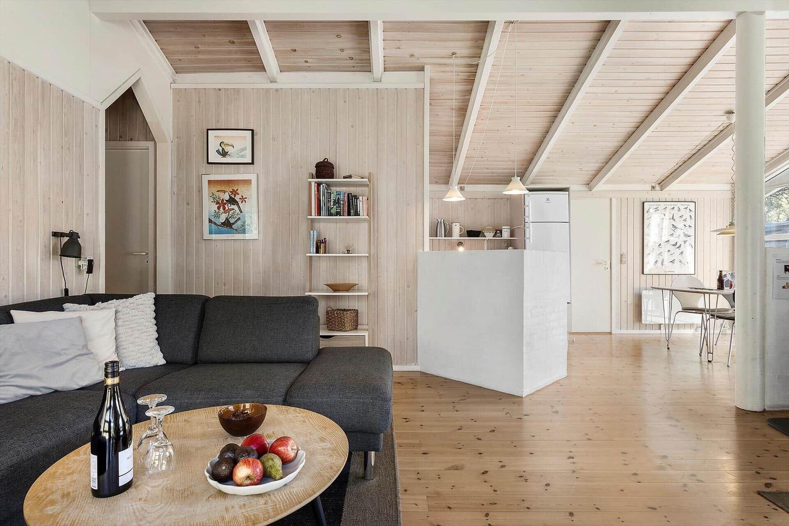 Wohnbereich mit Sofa, Tisch und Küchenbereich. Holzdecke und -boden.