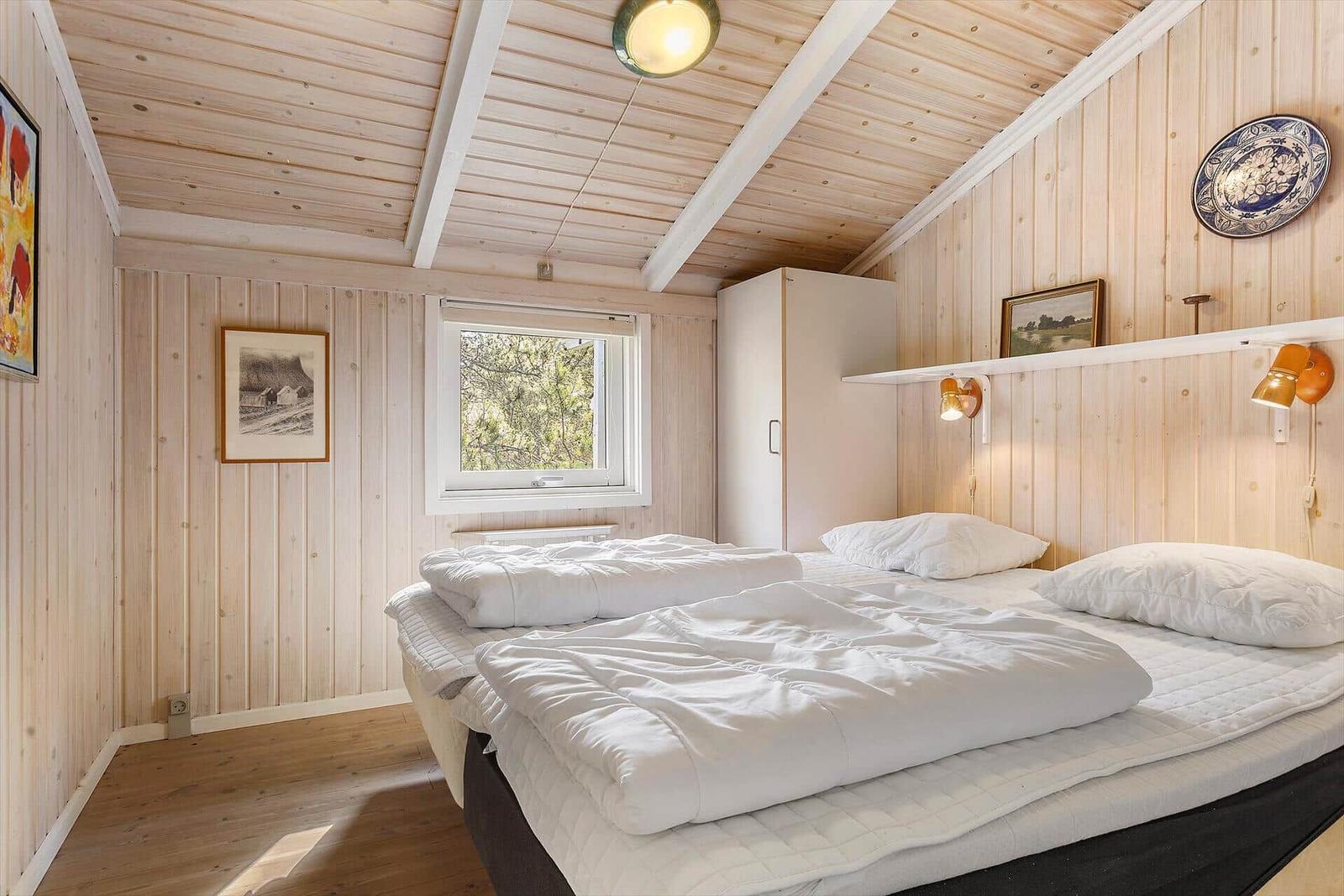 Schlafzimmer mit Holzwand, Bett, Fenster und Schrank.