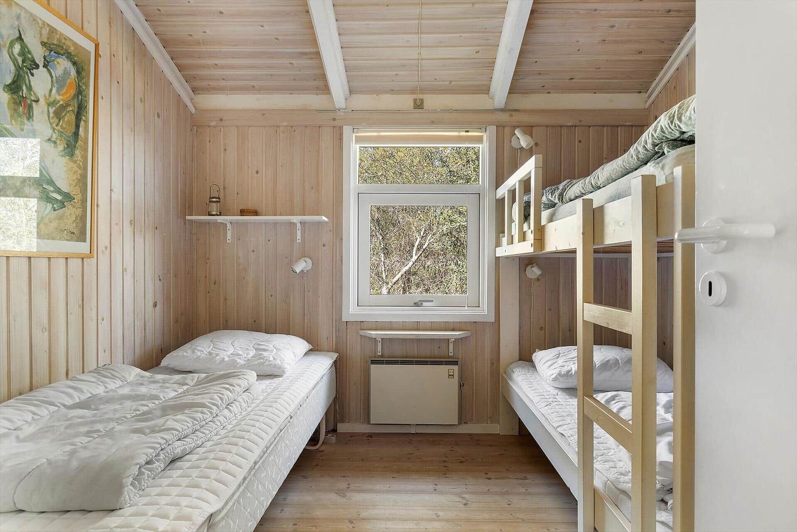 Zimmer mit Doppelstockbett und Einzelbett, Holzwand und Fenster mit Blick auf Bäume.
