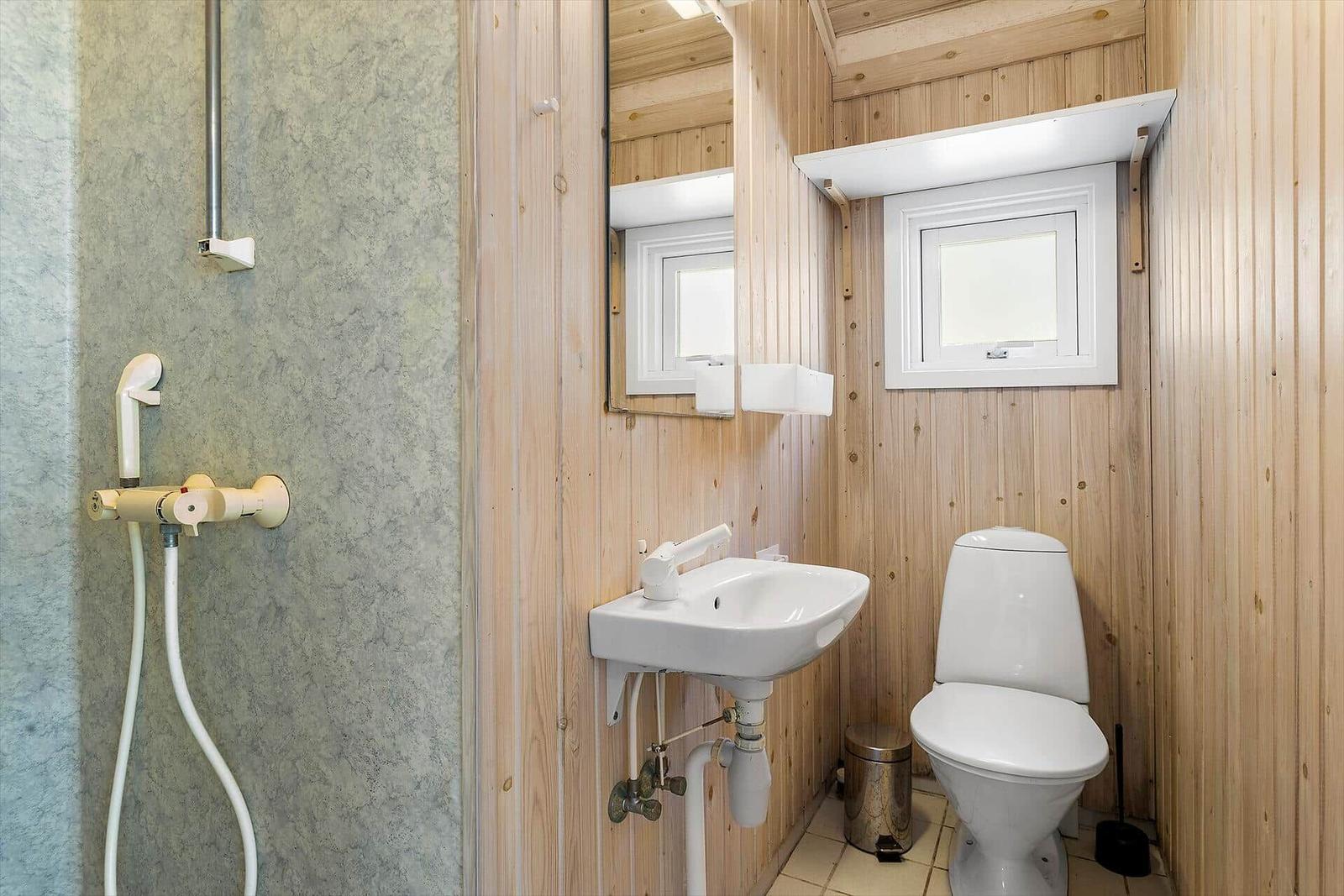 Bad mit Dusche, Waschbecken und Toilette. Holzwände und Fenster.