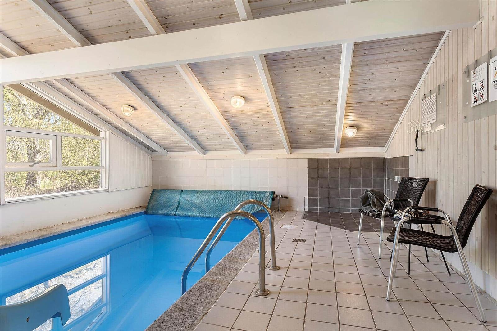 Innere Schwimmhalle mit Pool, Sitzgelegenheiten und Fenster zur Natur.