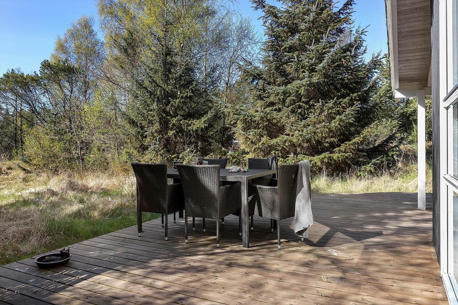 Terrasse mit Tisch und Stühlen, umgeben von Bäumen und Gras.