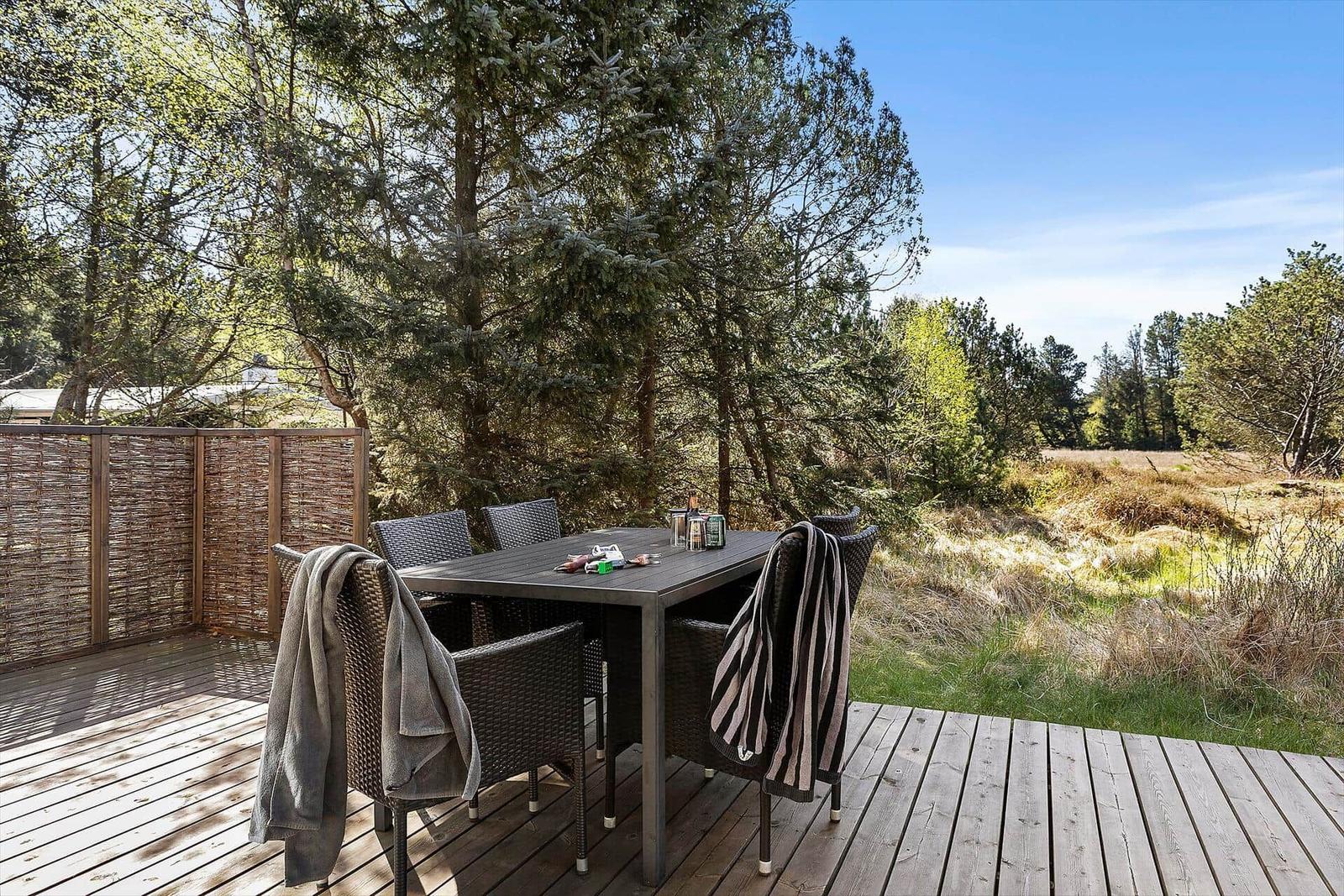 Terrasse mit Tisch und Stühlen, umgeben von Bäumen und Grasland.