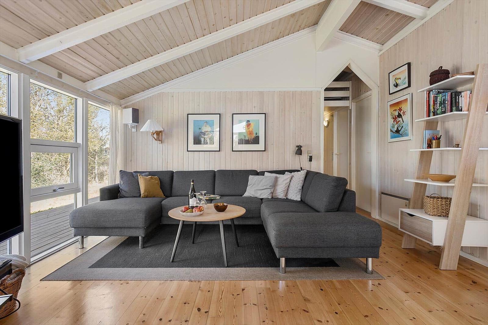 Wohnzimmer mit grauem Sofa, Holzboden und großen Fenstern.