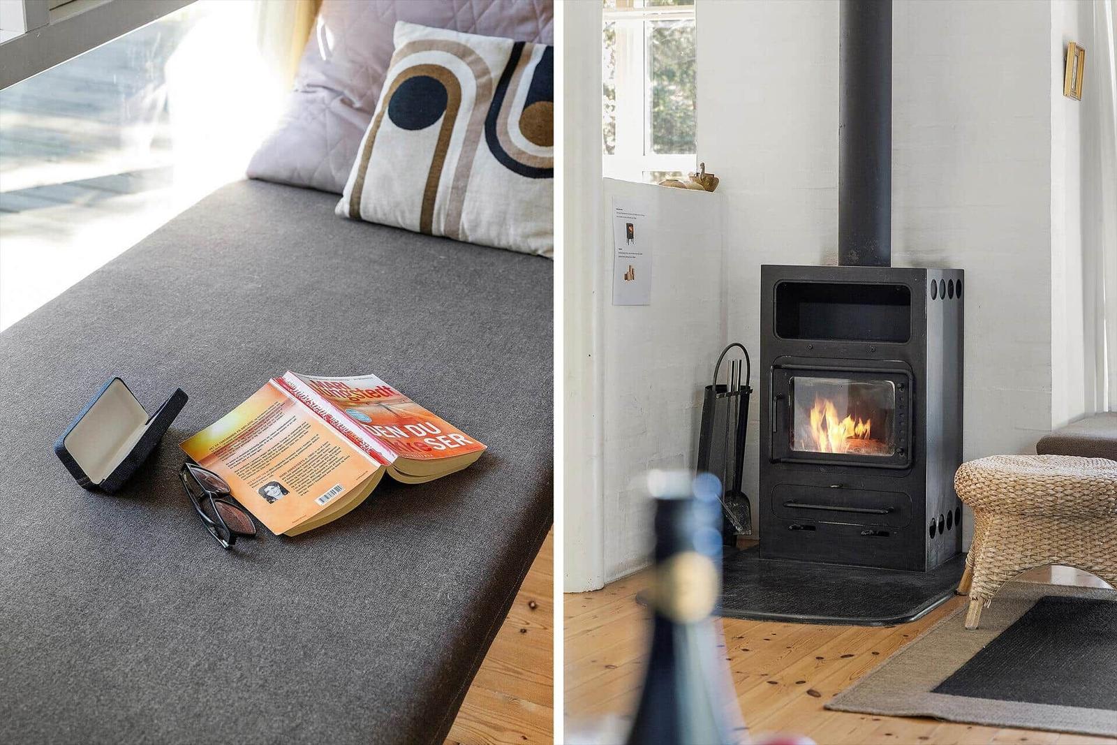 Sofa mit Kissen und Buch neben Kamin mit brennendem Holzofen.