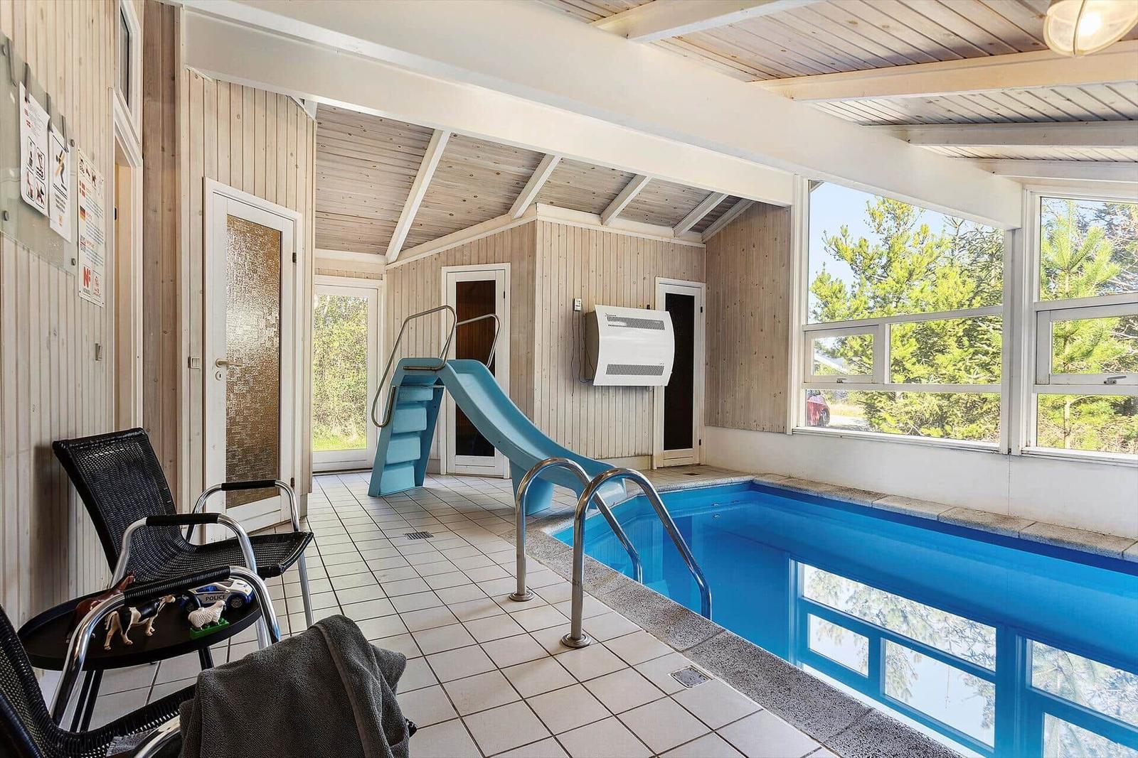 Innenpool mit Rutsche und Sitzgelegenheiten. Holzwände und große Fenster.