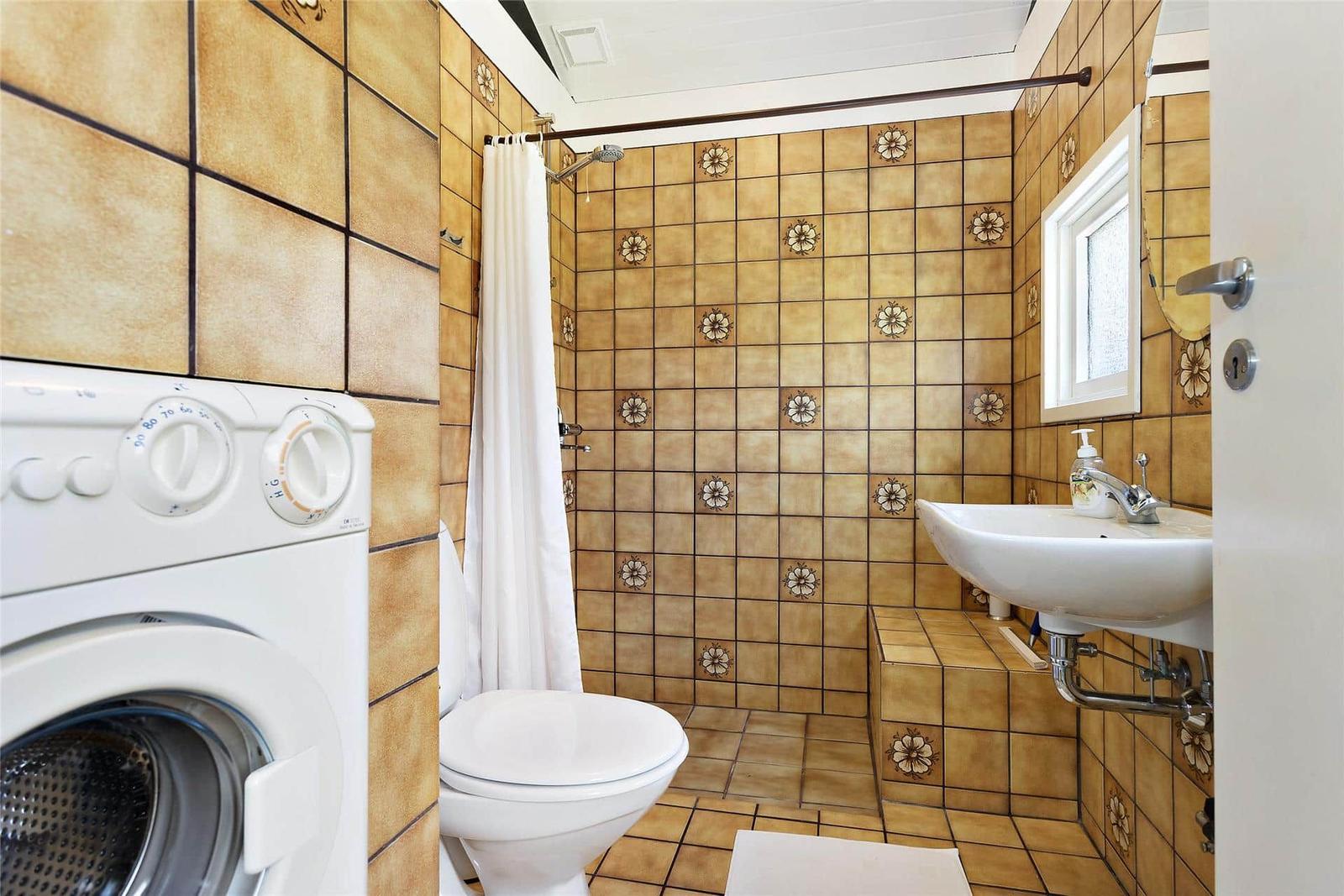 Bad mit Dusche, Waschmaschine und Toilette. Fliesen mit Blumenmuster.